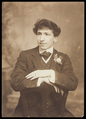 A man sitting backwards on a chair wearing formal attire. Photograph, 190-.