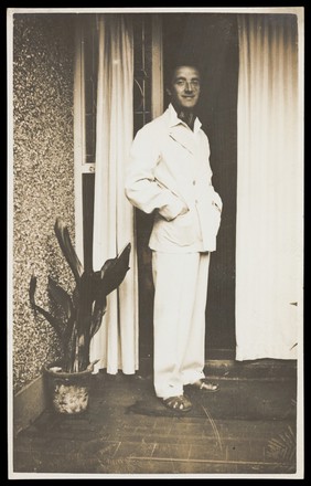 A man wearing a white suit poses by a doorway. Photographic postcard by Jerome Ltd., 192-.