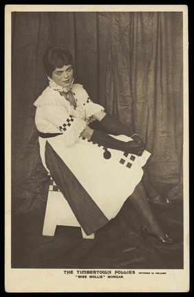 A British prisoner of war in drag, performing for "The Timbertown Follies", at a prisoner of war camp in Groningen. Photographic postcard, 191-.