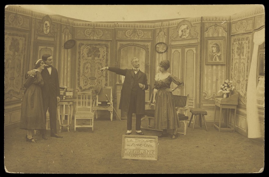 Amateur actors, some in drag, posing on stage for "Miquette & sa mere"; at Sennelager prisoner of war camp in Germany. Photographic postcard, 191-.