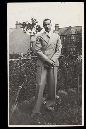 A man in a striped suit posing in a garden, holding a cigarette. Photographic postcard, 1939.