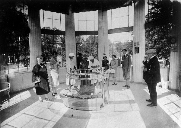 Franzensbad (Františkovy Lázně), Czechoslovakia: the interior of the Francis Spring where people stand to drink water drawn from the central circular point by female attendants in white uniforms and caps. Photograph.