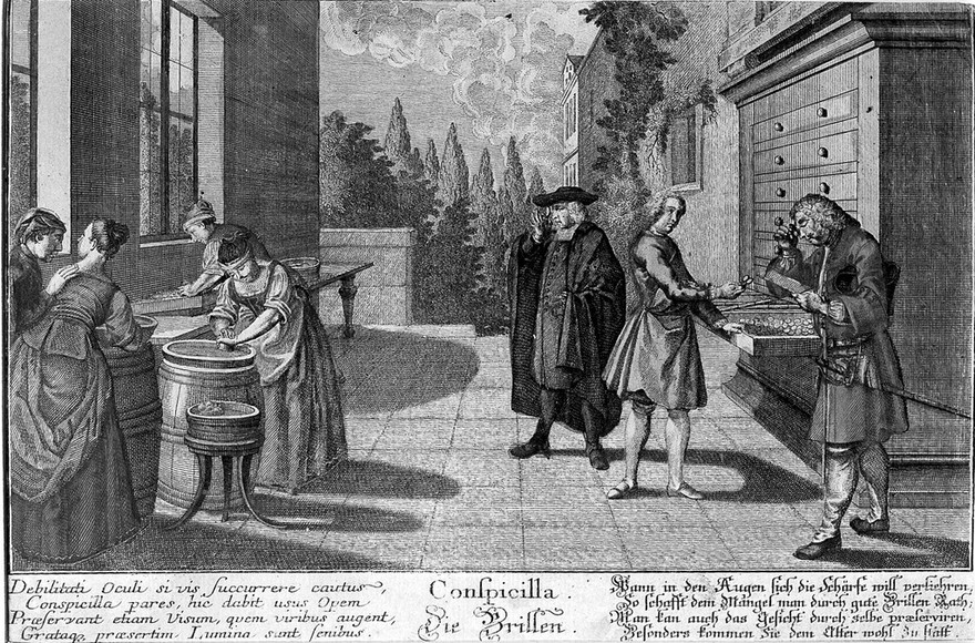 Women grind glass lenses while two customers try spectacles on. Coloured line engraving, 1799.