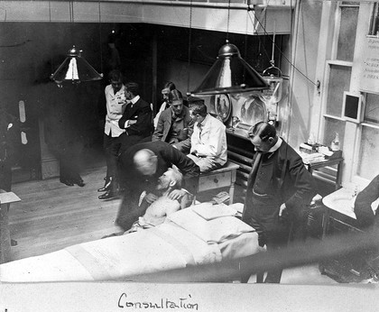 St Bartholomew's Hospital, London: doctors seeing to a sick man. Photograph, c. 1908.