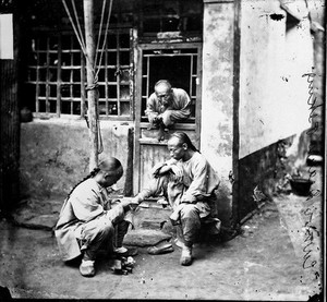 view A travelling chiropodist operating upon a corn on his patient's foot. Peking, Pechili province, China.