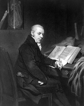 Portrait of Joshua Brookes, nearly whole-length, seated at desk with anatomical atlas on desk and specimen glass in background