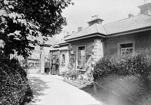 view Royal Portsmouth Hospital: the gate lodge, with the lodge-keeper and another person. Photograph, 1902.