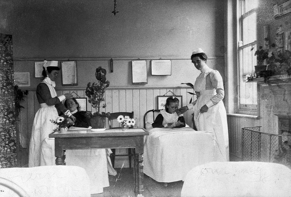 Part of a children's ward in a hospital with two nurses attending two children. Photograph.
