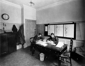 view Ambulance Column depot, 9 Gower Street, London: the Petrol Room, with two officials working at tables. Photograph, September 1918.