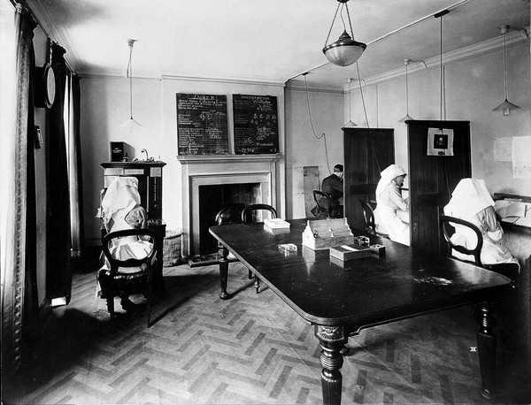Ambulance Column depot, 9 Gower Street, London: the Telephone Room, with officials in telephone booths, perhaps answering enquiries. Photograph, September 1918.