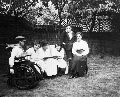 A physically disabled boy sitting in a wheelchair in a garden. Photograph, ca. 1910/1925.