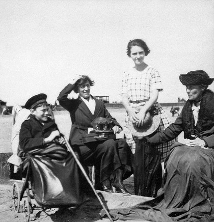 A physically disabled boy sitting in a wheelchair on a beach. Photograph, ca. 1910/1925.