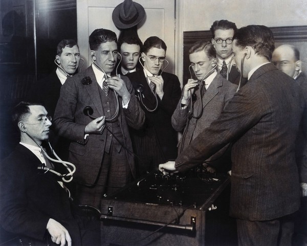 Doctors or medical students listening to their heartbeats using a multiple stethoscope. Photograph.