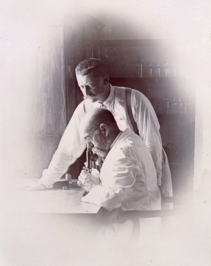 view Robert Koch and Richard Pfeiffer working in a laboratory, investigating the plague in Bombay. Photograph attributed to Captain C. Moss, 1897.