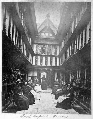 view Ford's Hospital, Coventry: residents seated in the courtyard looking toward the street. Photograph.