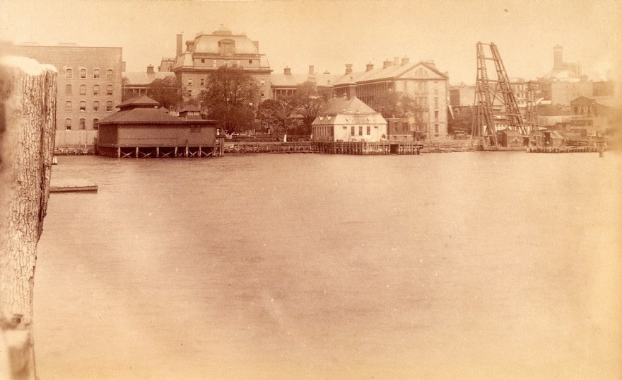 Bellevue Hospital, New York City: a wharf on the East River with buildings. Photograph.