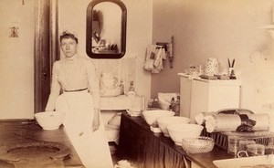 view Bellevue Hospital, New York City: a woman (nurse?) with bowls and cotton wool etc. on a sideboard. Photograph.