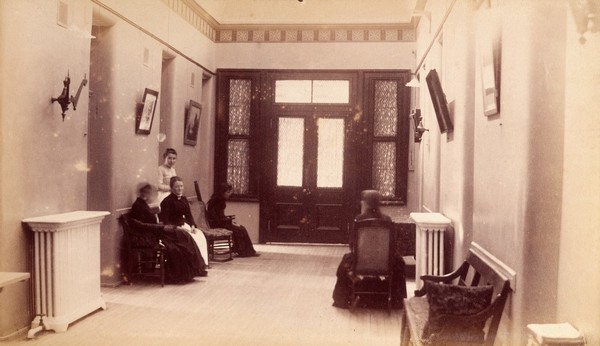 Bellevue Hospital, New York City: a corridor inside entrance to building, with seated women (patients?). Photograph.