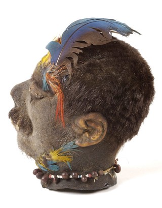 A Shuar shrunken head (tsantsa) from Ecuador with a stitched mouth and feather headdress.