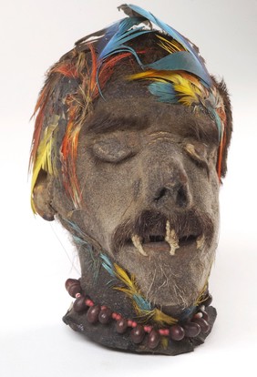 A Shuar shrunken head (tsantsa) from Ecuador with a stitched mouth and feather headdress.