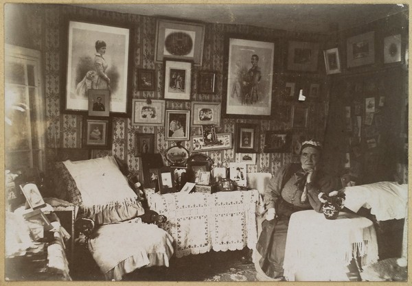 Nurse Tremlow (name unconfirmed), a monthly nurse to gentry and royal households, in retirement, with photographs of her employers. Photograph, 19--.