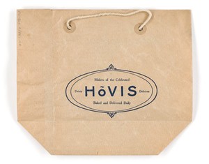 view The most appetising bread : Hovis, the national health builder / [Hovis Ltd.] Brown paper bag with string handles. An illustration of a loaf of Hovis wholemeal bread is printed in dark blue on one side and a slogan in a decorative oval border is on the reverse.