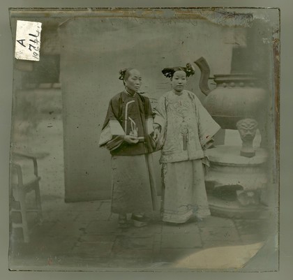 China: a Manchu lady with her maid standing beside a bronze burner, Beijing. Photograph by John Thomson, 1869.