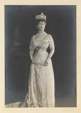 Queen Mary (May of Teck) standing, wearing a tiara and holding a folded fan. Photograph by John Thomson, ca. 1910.