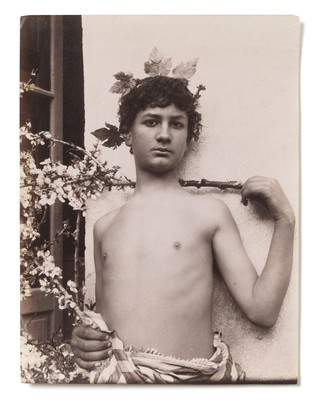 A Sicilian boy, naked from the waist up, his hand level with his shoulder, crowned with leaves. Photograph by W. von Gloeden, 1901.