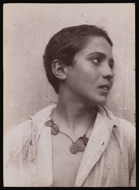 A Sicilian boy, head and shoulders, with a necklace of coins. Photograph by W. von Gloeden, 1900.