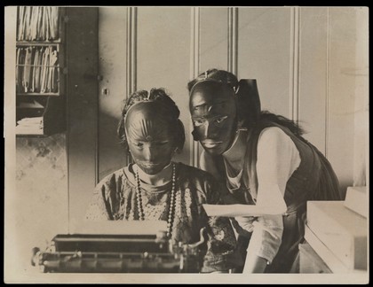 Rubber beauty masks, worn to remove wrinkles and blemishes; modelled by two women at a typewriter. Photograph, ca. 1921.