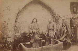 view Santorini, Greece: men carrying hogskins full of water to a cistern. Photograph. 18--.