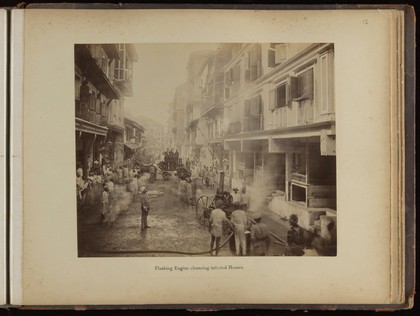 Groups of men on a street spraying jets of water into plague infected houses, during the epidemic of plague in Bombay. Photograph attributed to Captain C. Moss, 1897.