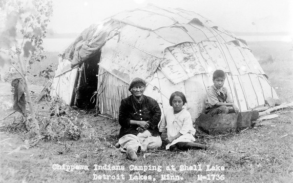 Chippewa Indians camping at Shell Lakes, Detroit Lakes, Minnesota. Three figures outside a hut.