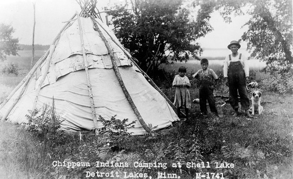 Chippewa Indians camping at Shell Lakes, Detroit Lakes, Minnesota. Man, dog and two children outside a hut.