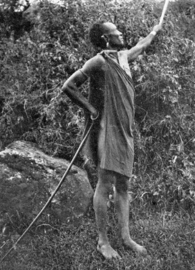 Dorako man making medicine and prevent the rain from falling, whistling and defying the rain gods, holding his sword upright and gently rubbing the handle. Katla, South Africa