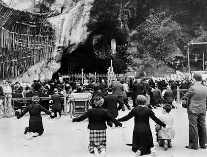 Pilgrims kneeling before shrine of our Lady of Lourdes.