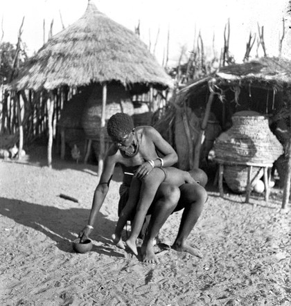 M0006587: Kwanyama woman giving an enema to a boy / M0006587EA: Kwanyama woman giving an enema to a boy / M0006587EB: Kwanyama woman giving an enema to a boy / M0006588: Kwanyama woman giving an enema to a boy
