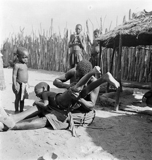 view Angola: a Kwanyama woman performing an enema on a small child: the woman introduces liquid into the rectum. Photograph by Antoinette Powell-Cotton, 1936/1937.