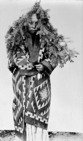 Salish girl wearing the fir boughs and goat's wool blanket that signify her adolescence