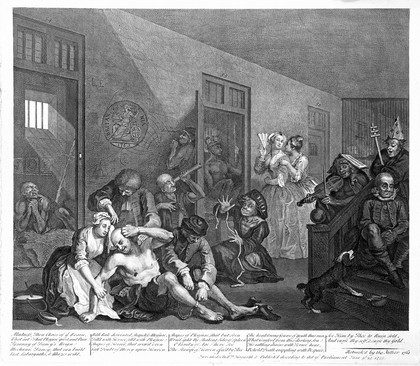 An insane man (Tom Rakewell) sits on the floor manically grasping at his head, his lover (Sarah Young) cries at the spectacle while two attendants attach chains to his legs; they are surrounded by other lunatics at Bethlem hospital, London. Engraving by W. Hogarth, 1763.