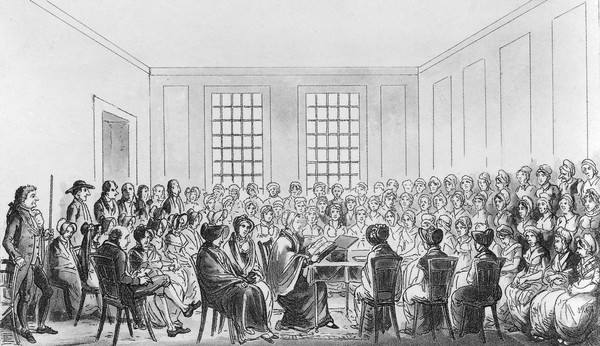 Elizabeth Fry is seated at a table in Newgate Prison, London, surrounded by women prisoners listening to her. Etching and aquatint.