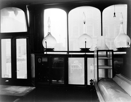 Late 19th century chemist's shop formerly owned by N.F. Tyler. At 87 Abingdon Road, Kensington W 8. Photograph by Mr Michieli showing the view of the front window and door with carboys in position.