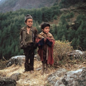view Nepal; Sherpa children of the Khumbu, 1986. Two smiling children share an amusing moment in the village of Phakding (altitude 3000 metres). Their clothing highlights the poverty of some of the Sherpa families.