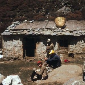 view Nepal; herdsmen of the Khumbu, 1986. Three herdsmen stop for refreshments at the Shomare Hotel. The sign above the door of this tea shop reads: 'Wel-come to Shomare Hotel', evidence that westerners pass the door en rout to the high mountains.