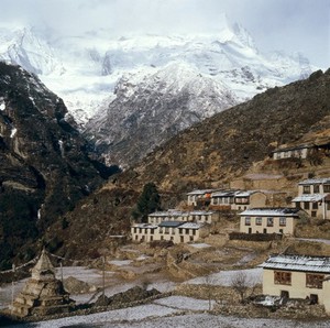 view Nepal; town life in the Khumbu, 1986. Namche Bazar (altitude 3446 metres), a bustling and prosperous market town, is the largest Sherpa settlement in the Khumbu. Many of its Tibetan-style houses devote the ground floor to animal shelters while the family lives upstairs. Most have windows and doors at the front of the building only, the back being built into the side of the mountain. Firewood is stacked against walls, and small terraced fields grow staples (potatoes, barley, wheat). At left is a Buddhist shrine or stupa, on each side of which is painted the eyes of the Buddha. Prayer flags are strung out from its summit.