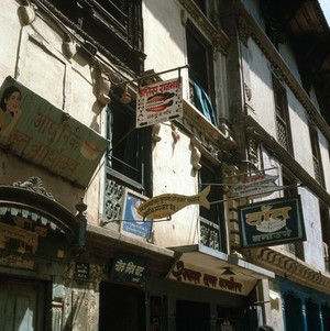 view Nepal; street of dentists, Kathmandu 1986. In 1982, there were 17 government-trained dental surgeons in Nepal, some of whom practised in this street. For those too fearful or who could not afford to visit one of these surgeries, a nearby shrine was dedicated to Vaisha Dev, the god of toothache. Surrounding the god was a plank of wood into which thousands of nails had been driven. Planting a nail was believed to get rid of toothache by pinning down all evil spirits and influences.