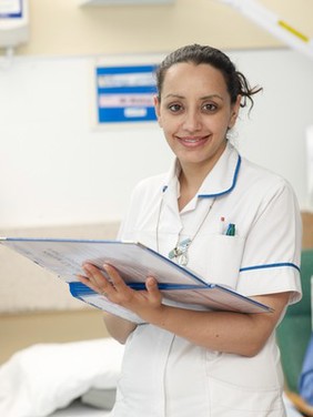 Smiling female nurse on hospital ward with patient notes