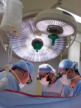 Three male surgeons operating under theatre lights, UK