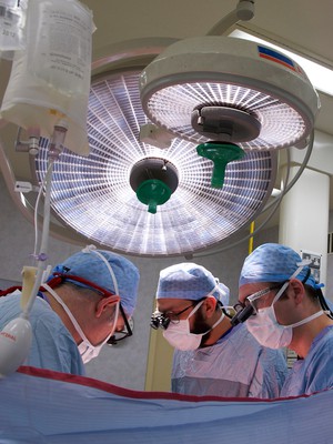 view Three male surgeons operating under theatre lights, UK